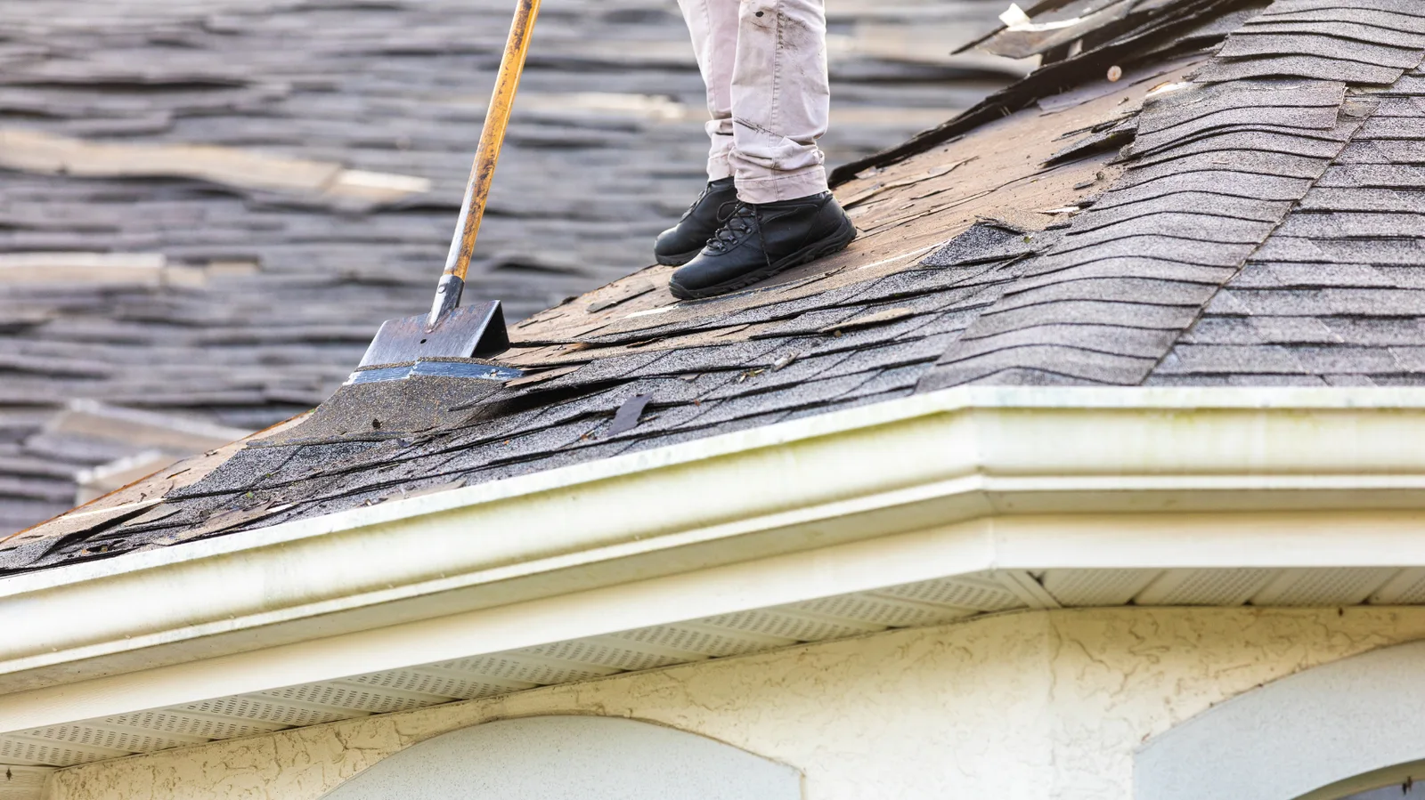 Roofer standing at a roof edge with a shovel wedged under shingles